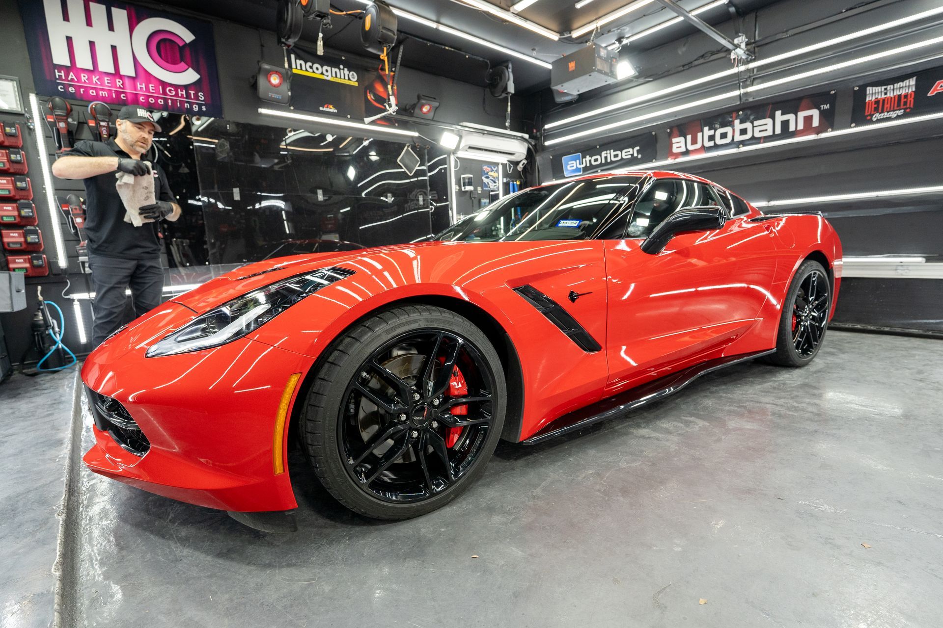 A man is cleaning a red sports car in a garage.