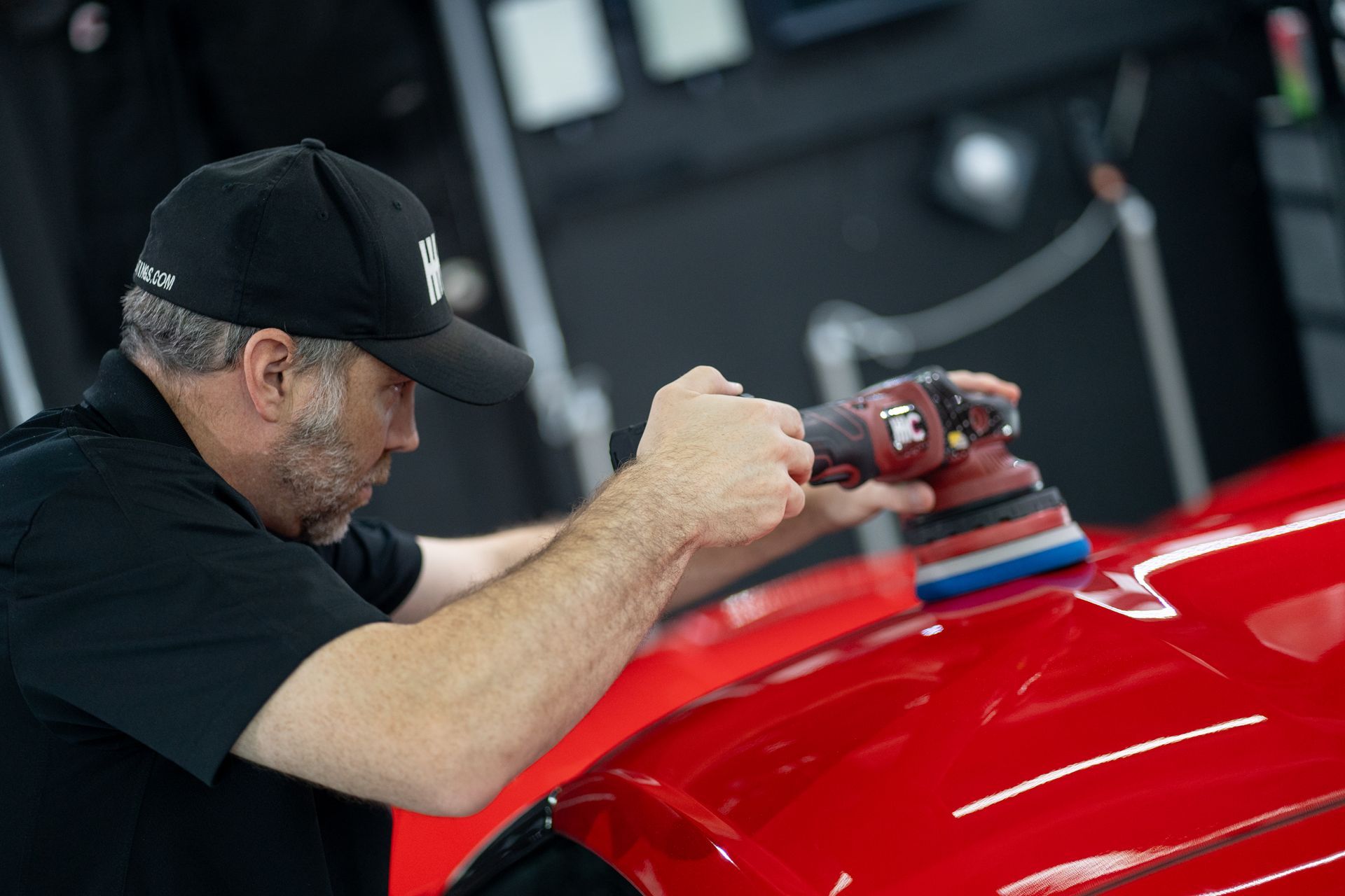 A man is polishing a red car with a machine.