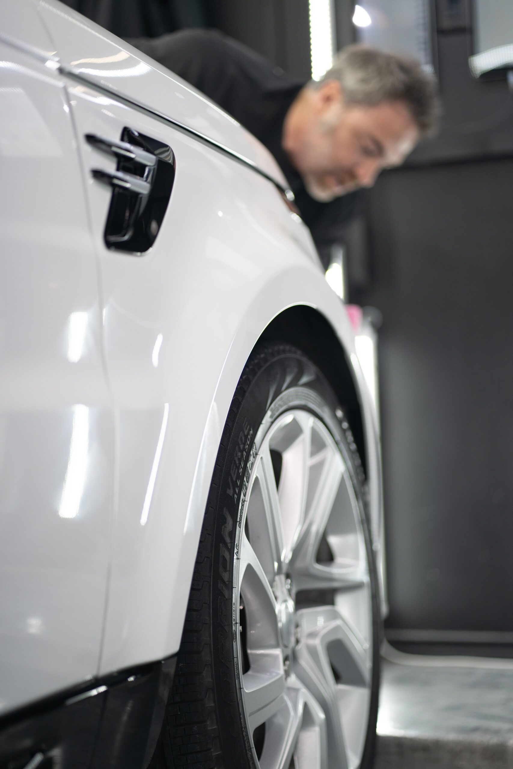 A man is looking at the fender of a white car.