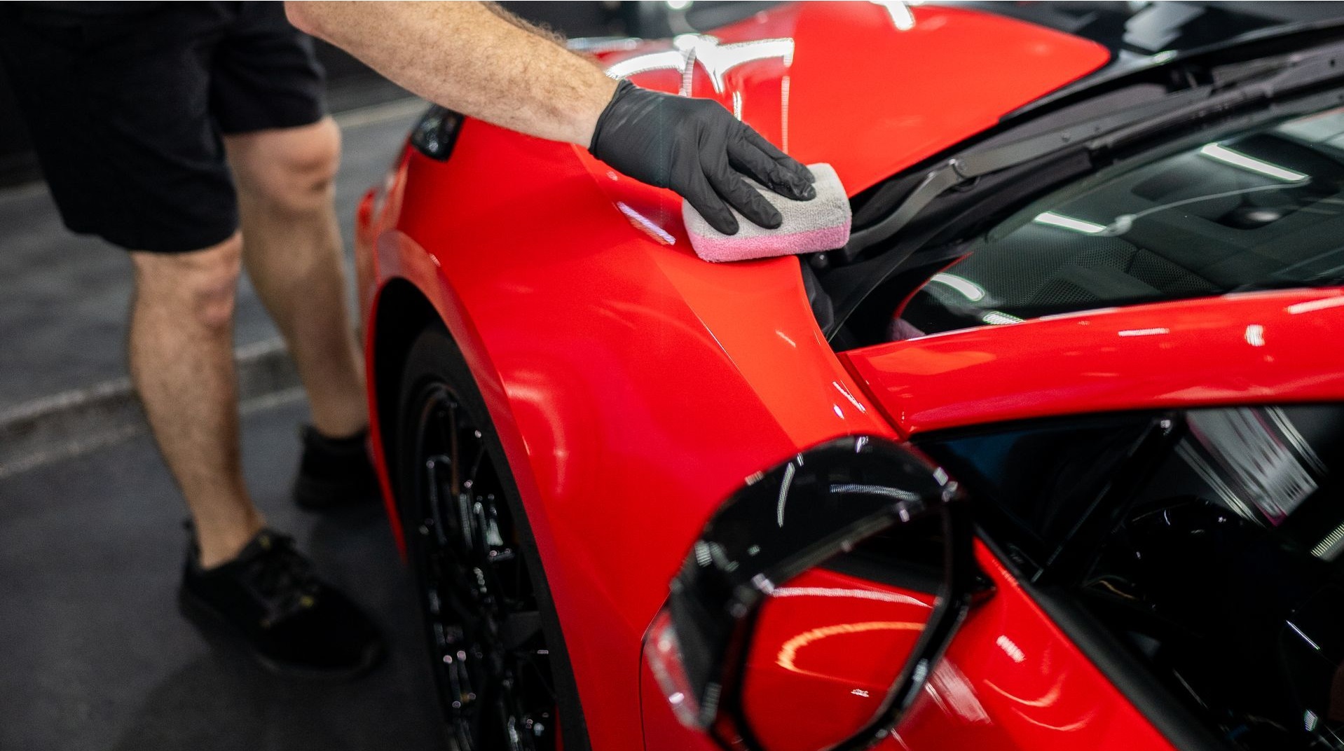 A man is polishing a red sports car in a garage.