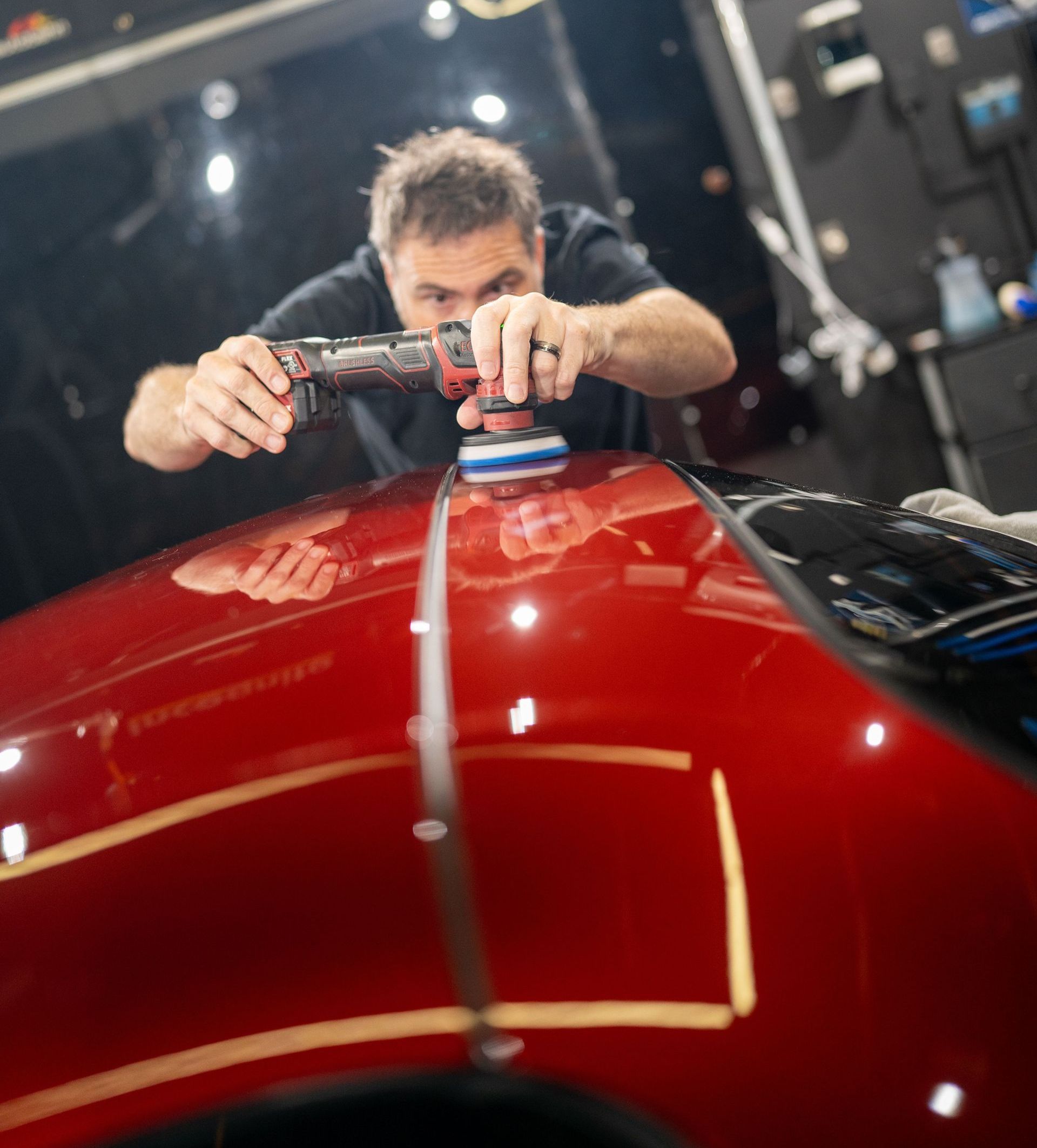 A man is polishing the hood of a red car.