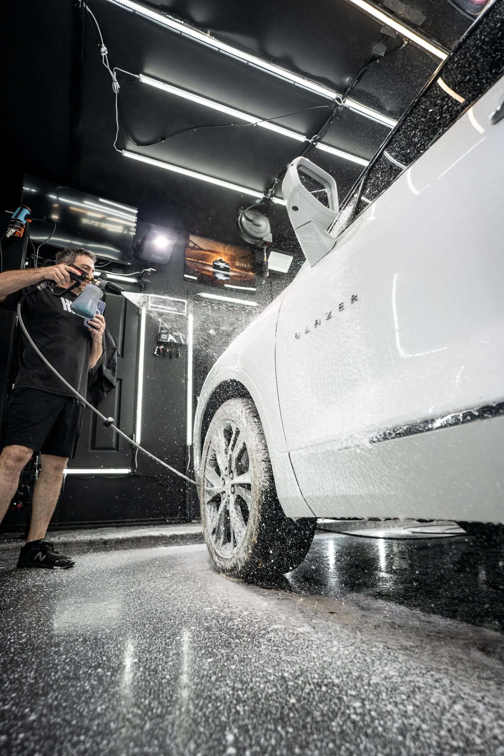 A man is washing a white car in a garage.