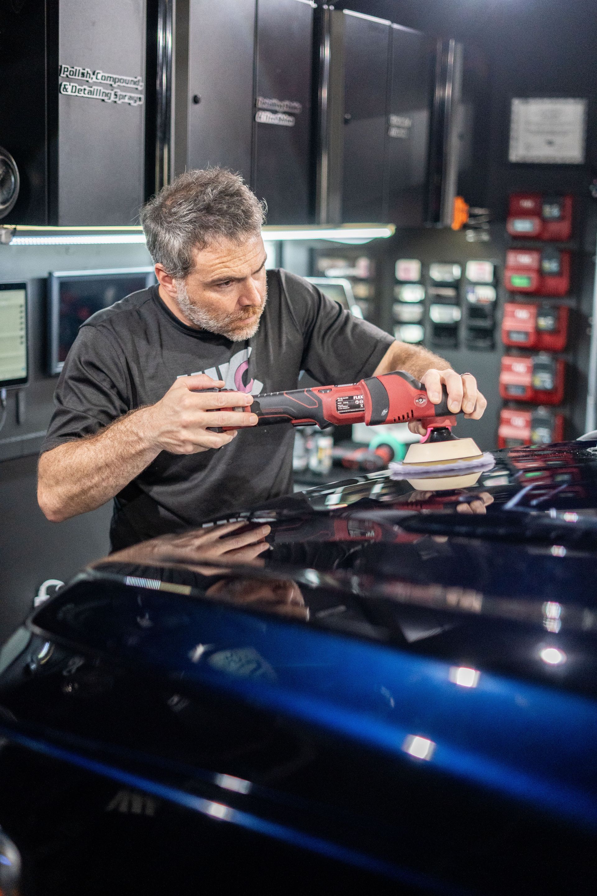 A man is polishing the hood of a car in a garage.